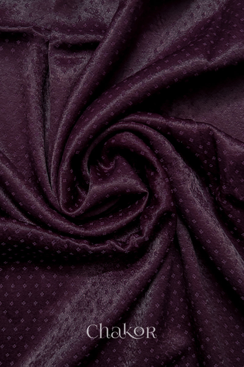 Close-up of dark burgundy mashru self textured fabric arranged in a swirling design with 'Chakor' logo visible.