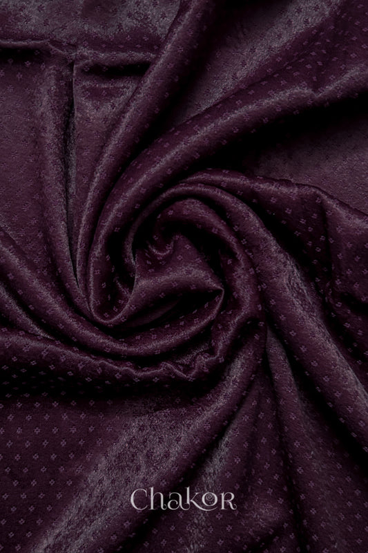 Close-up of dark burgundy mashru self textured fabric arranged in a swirling design with 'Chakor' logo visible.