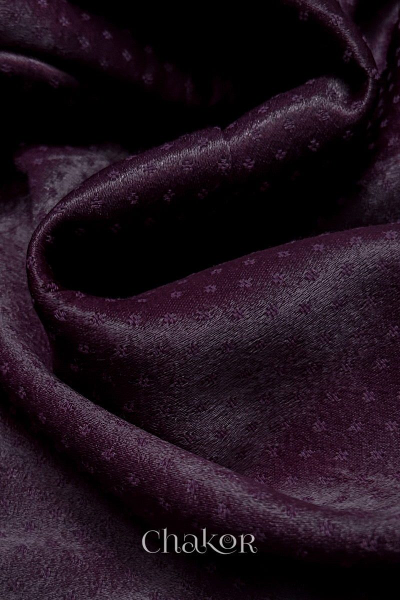 Close-up of dark burgandy mashru self textured fabric with 'Chakor' logo visible.