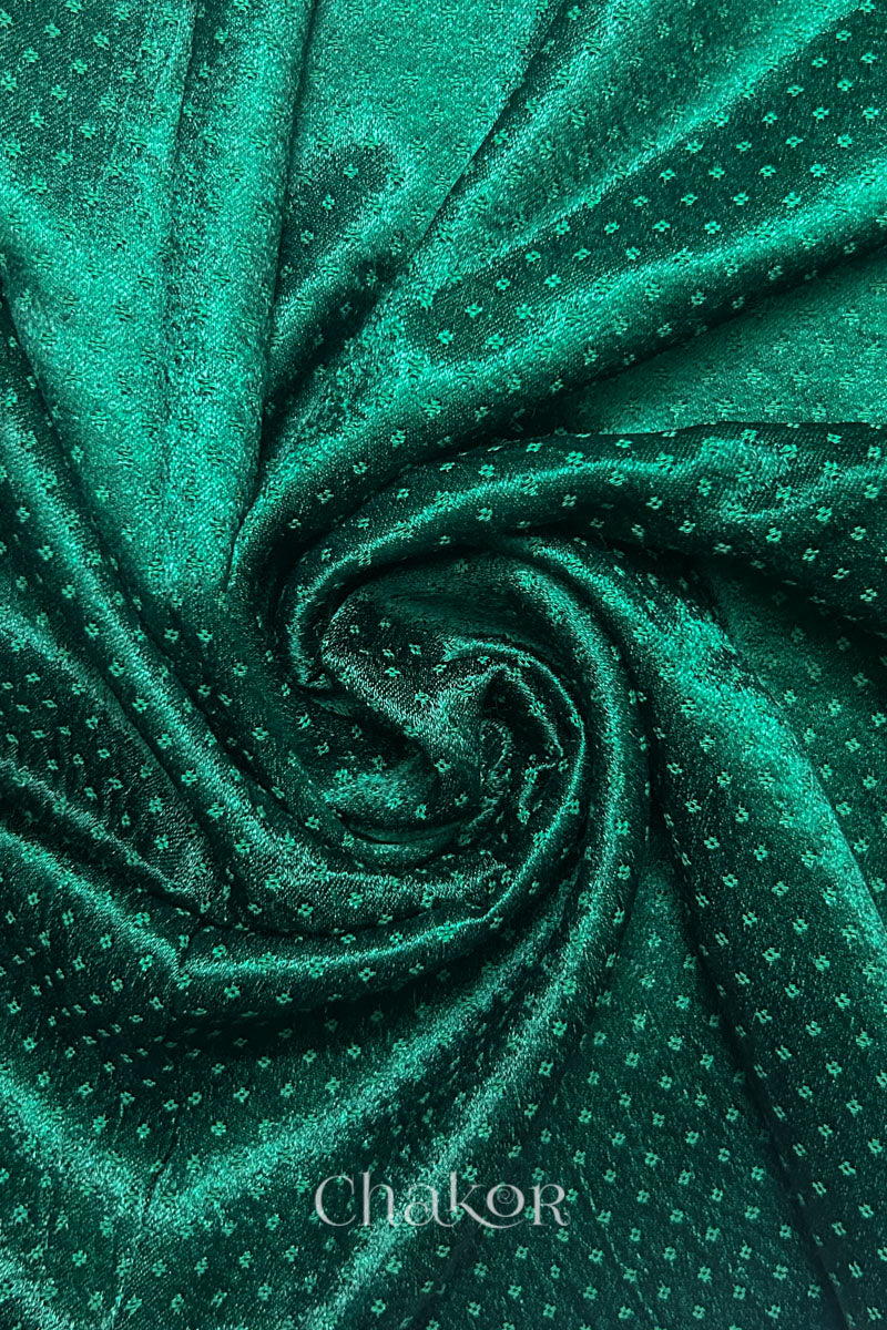 Close-up of dark green mashru self textured fabric arranged in a swirling design with 'Chakor' logo visible.
