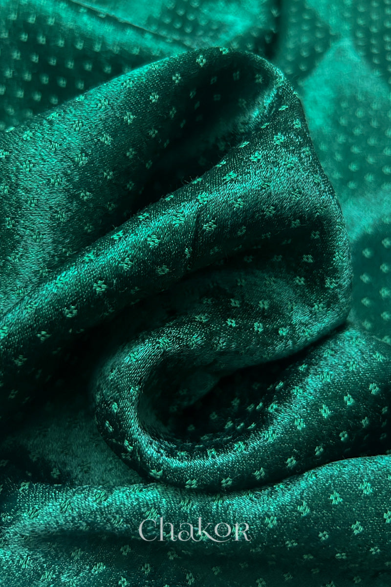 Close-up of dark green mashru self textured fabric with 'Chakor' logo visible.
