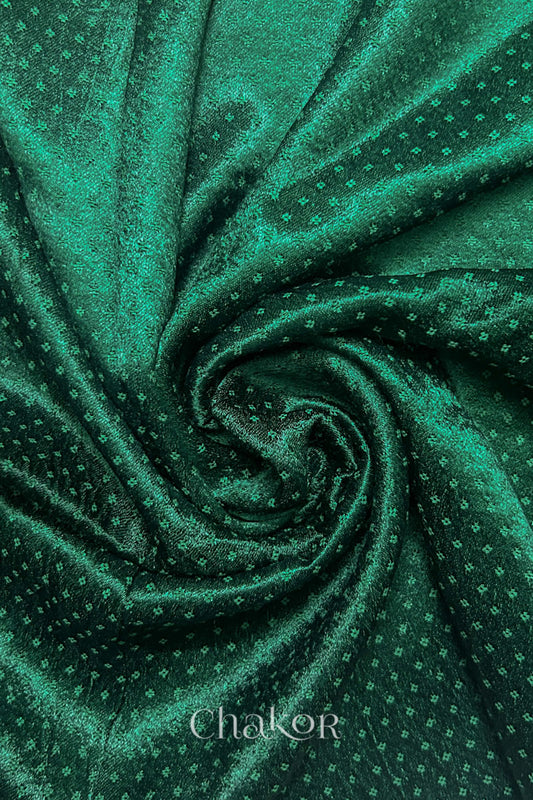 Close-up of dark green mashru self textured fabric arranged in a swirling design with 'Chakor' logo visible.
