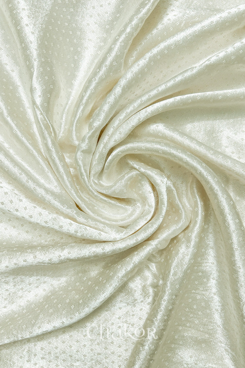 Close-up of off-white mashru self textured fabric arranged in a swirling design with 'Chakor' logo visible.