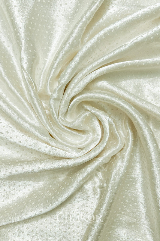 Close-up of off-white mashru self textured fabric arranged in a swirling design with 'Chakor' logo visible.
