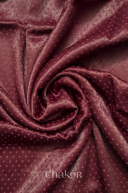 Close-up of maroon mashru self textured fabric arranged in a swirling design with 'Chakor' logo visible.

