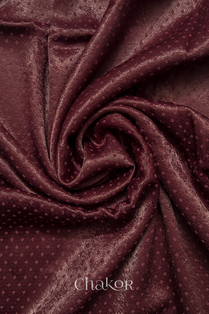Close-up of maroon mashru self textured fabric arranged in a swirling design with 'Chakor' logo visible.

