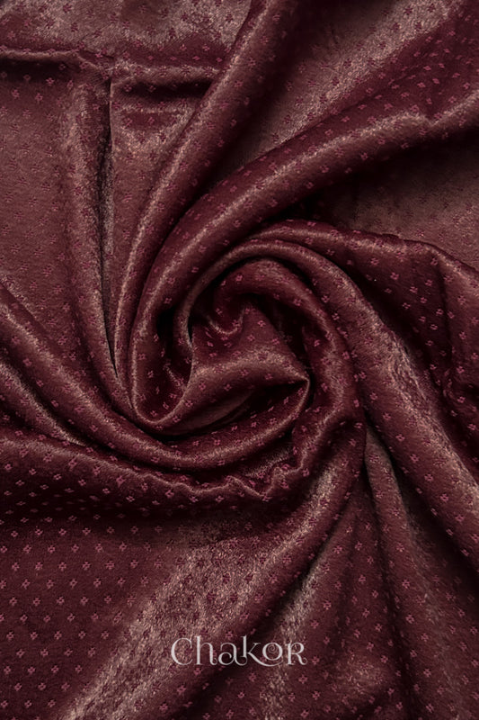Close-up of maroon mashru self textured fabric arranged in a swirling design with 'Chakor' logo visible.

