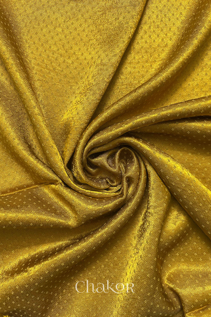Close-up of mustard yellow mashru self textured fabric arranged in a swirling design with 'Chakor' logo visible.
