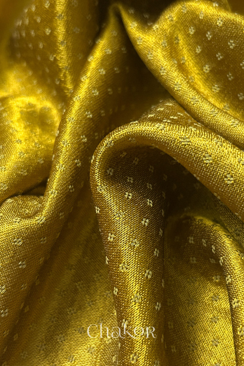 Close-up of mustard yellow mashru self textured fabric with 'Chakor' logo visible.

