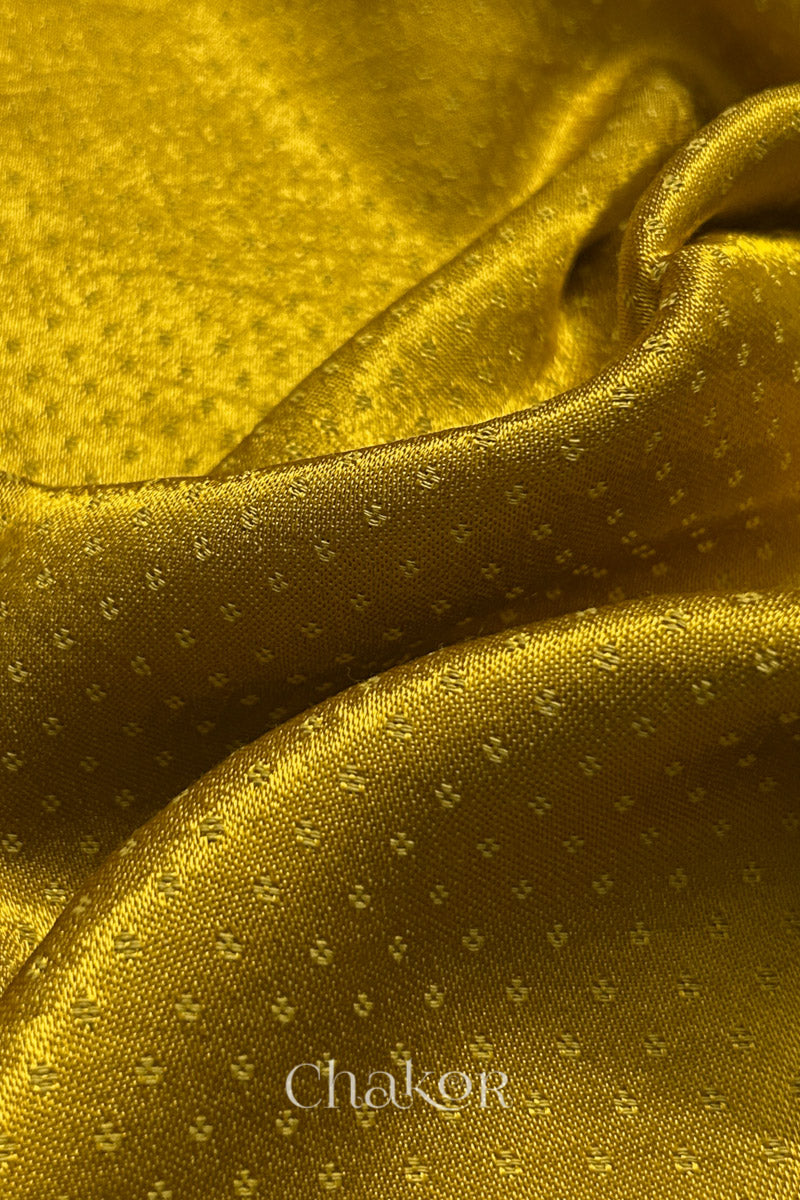Close-up of mustard yellow mashru self textured fabric with 'Chakor' logo visible.