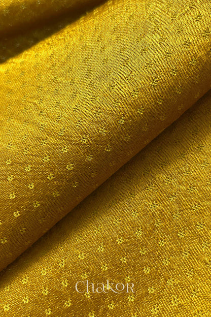 Close-up of mustard yellow mashru self textured fabric with 'Chakor' logo visible.
