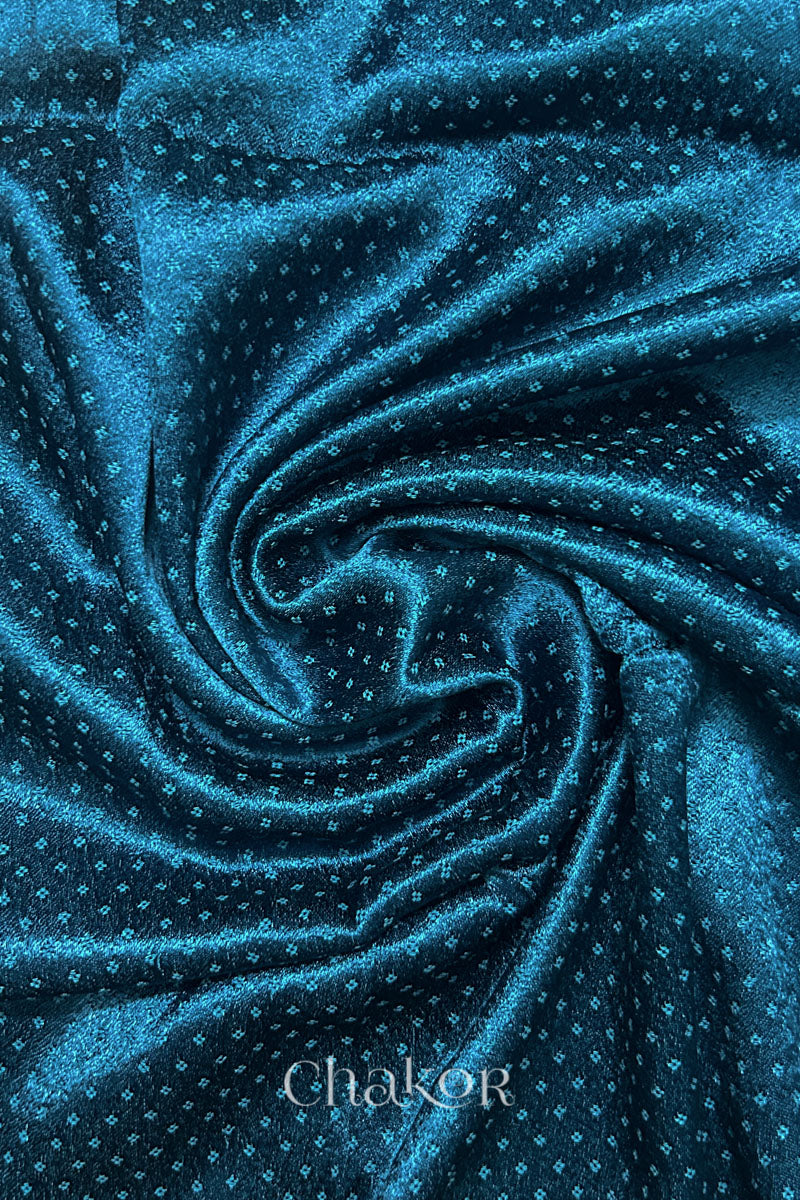 Close-up of deep indigo mashru self textured fabric arranged in a swirling design with 'Chakor' logo visible.
