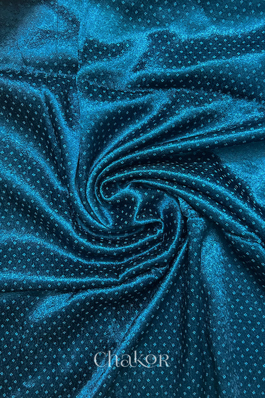 Close-up of deep indigo mashru self textured fabric arranged in a swirling design with 'Chakor' logo visible.
