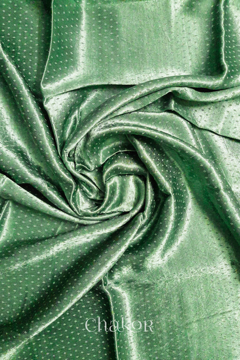 Close-up of pista green mashru self textured fabric arranged in a swirling design with 'Chakor' logo visible.