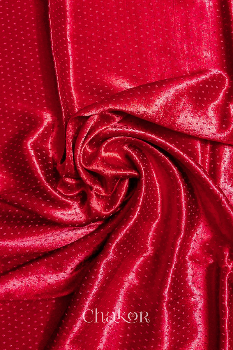 Close-up of red mashru self textured fabric arranged in a swirling design with 'Chakor' logo visible.