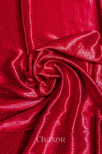 Close-up of red mashru self textured fabric arranged in a swirling design with 'Chakor' logo visible.