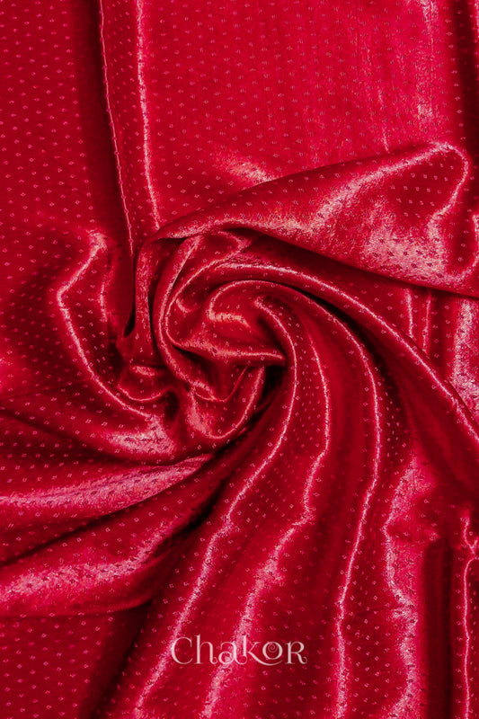 Close-up of red mashru self textured fabric arranged in a swirling design with 'Chakor' logo visible.