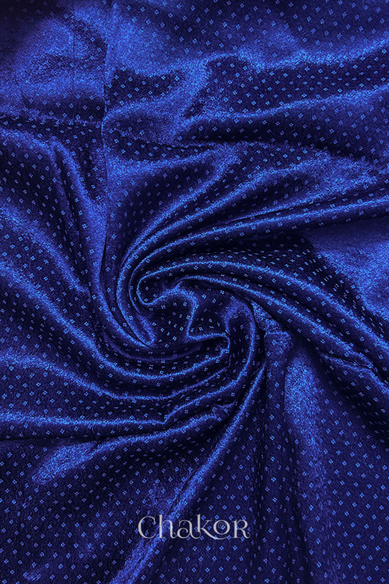 Close-up of royal blue mashru self textured fabric arranged in a swirling design with 'Chakor' logo visible.