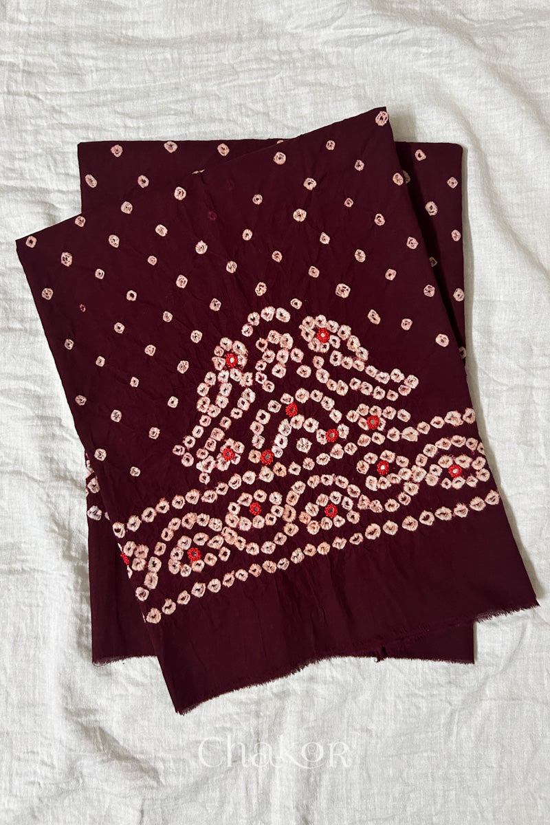 Maroon Kutch Bandhani cambric cotton unstitched blouse piece folded on white fabric.
