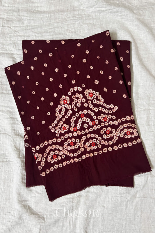 Maroon Kutch Bandhani cambric cotton unstitched blouse piece folded on white fabric.
