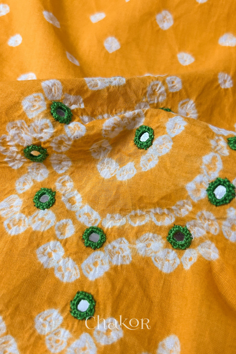 Close-up of yellow Kutch Bandhani blouse fabric showing Keri motifs and hand-embroidered mirror work.
