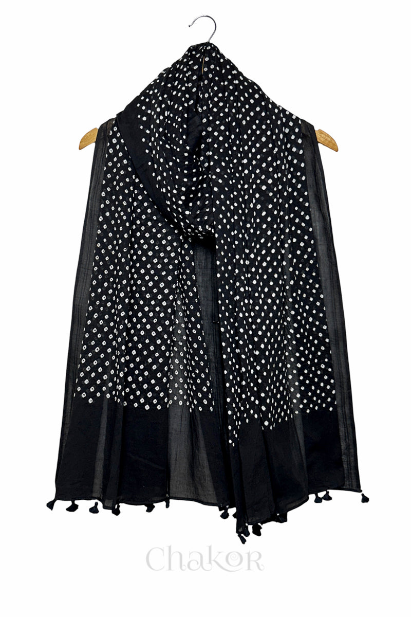 Chakor's black cotton dupatta adorned with white bandhani dots, draped elegantly on a wooden hanger, featuring tassels at the edge.