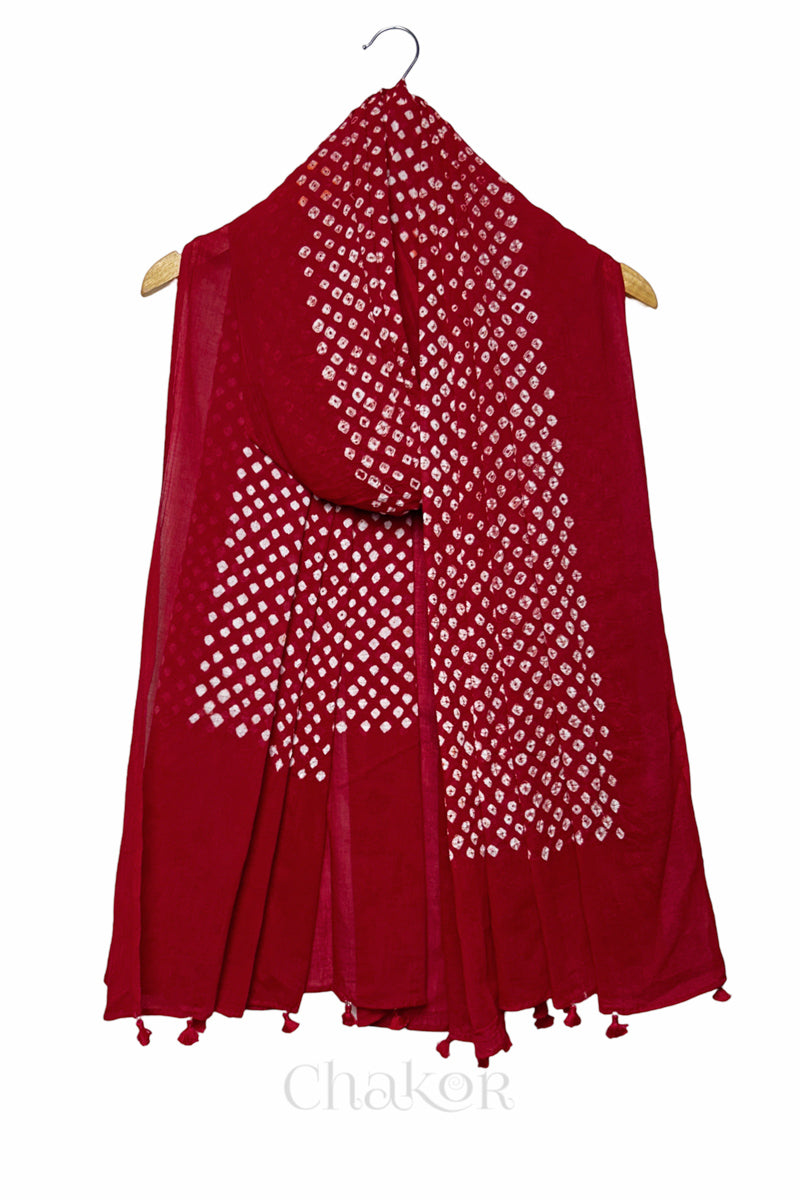 Chakor's red cotton dupatta adorned with white bandhani dots, draped elegantly on a wooden hanger, featuring tassels at the edge.