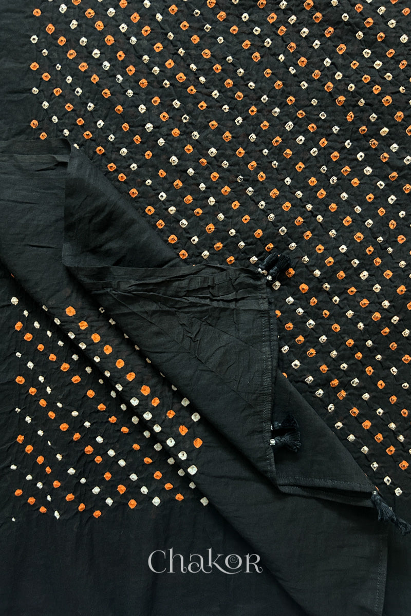 Close up of Authentic Black Bandhani dupatta featuring handmade tassels and dense white & orange tie-dye dot pattern by CHAKOR.