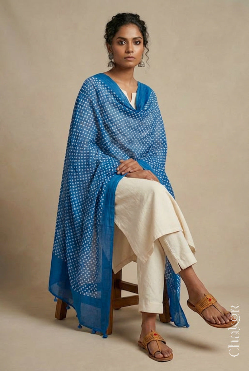 Model wearing indigo bandhani mul cotton dupatta edged with tassels on an offwhite kurta set.