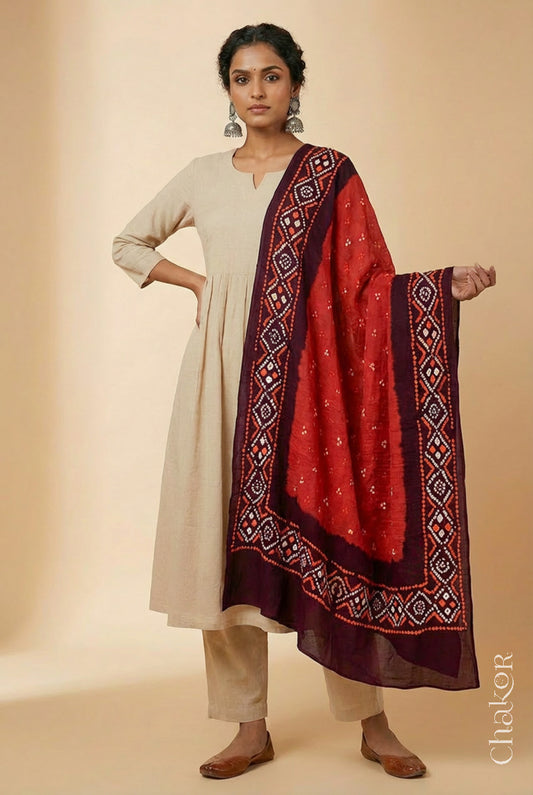 Model wearing rust and maroon Bandhani mul cotton dupatta with tie-dye dot pattern and pallu edged with tassels draped over a white kurta.