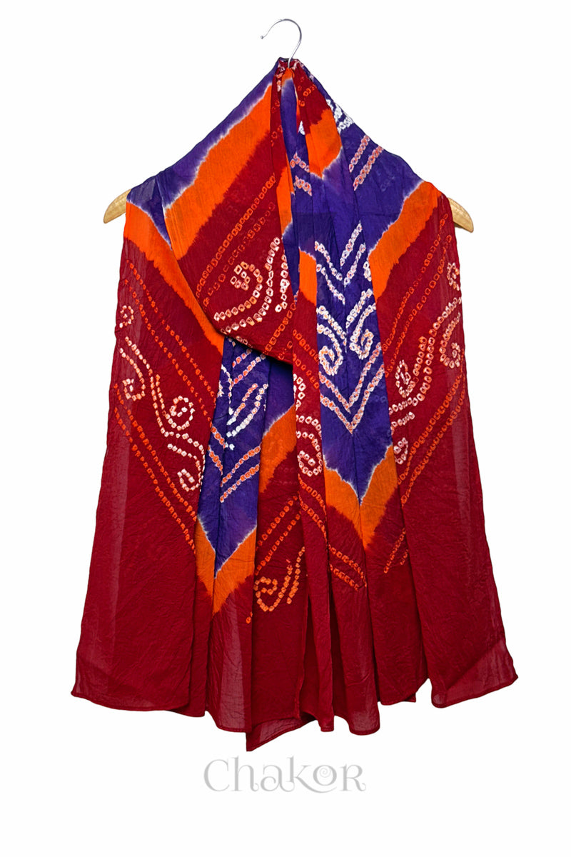 Red and purple Bandhani mul cotton dupatta draped on hanger showing multicolour tie-dye bands and patterned layout.