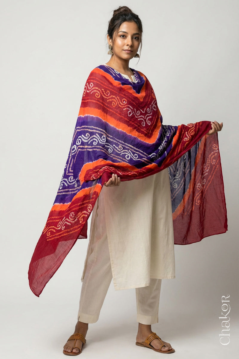 Model wearing red purple mul cotton Bandhani dupatta with multicolour tie-dye dots and striped bands draped over a white kurta.