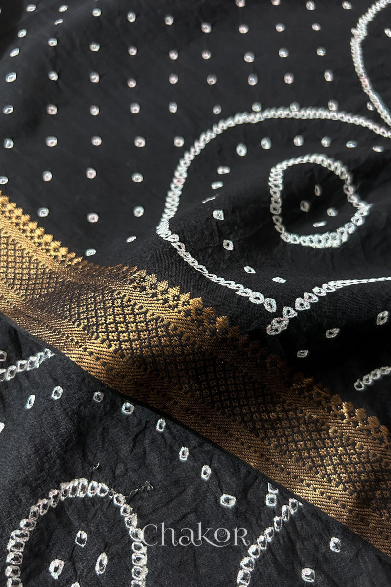 Close-up of white pearl-like dots and golden zari border detail in the Black Kutch Bandhani tie-dye pattern.
