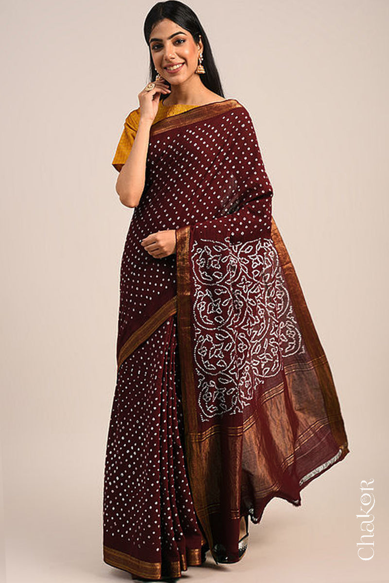 Woman wearing a maroon bandhani saree with traditional bandhej designs and zari border pallu.