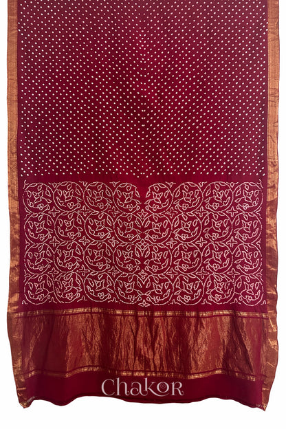 Red saree, flat draped with Rai Bandhej traditional design against white background and 'Chakor' watermark.
