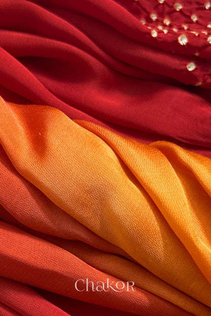 Close-up of bandhani stole featuring ombre dyeing in orange & red on lustrous modal fabric with 'Chakor' branding.
