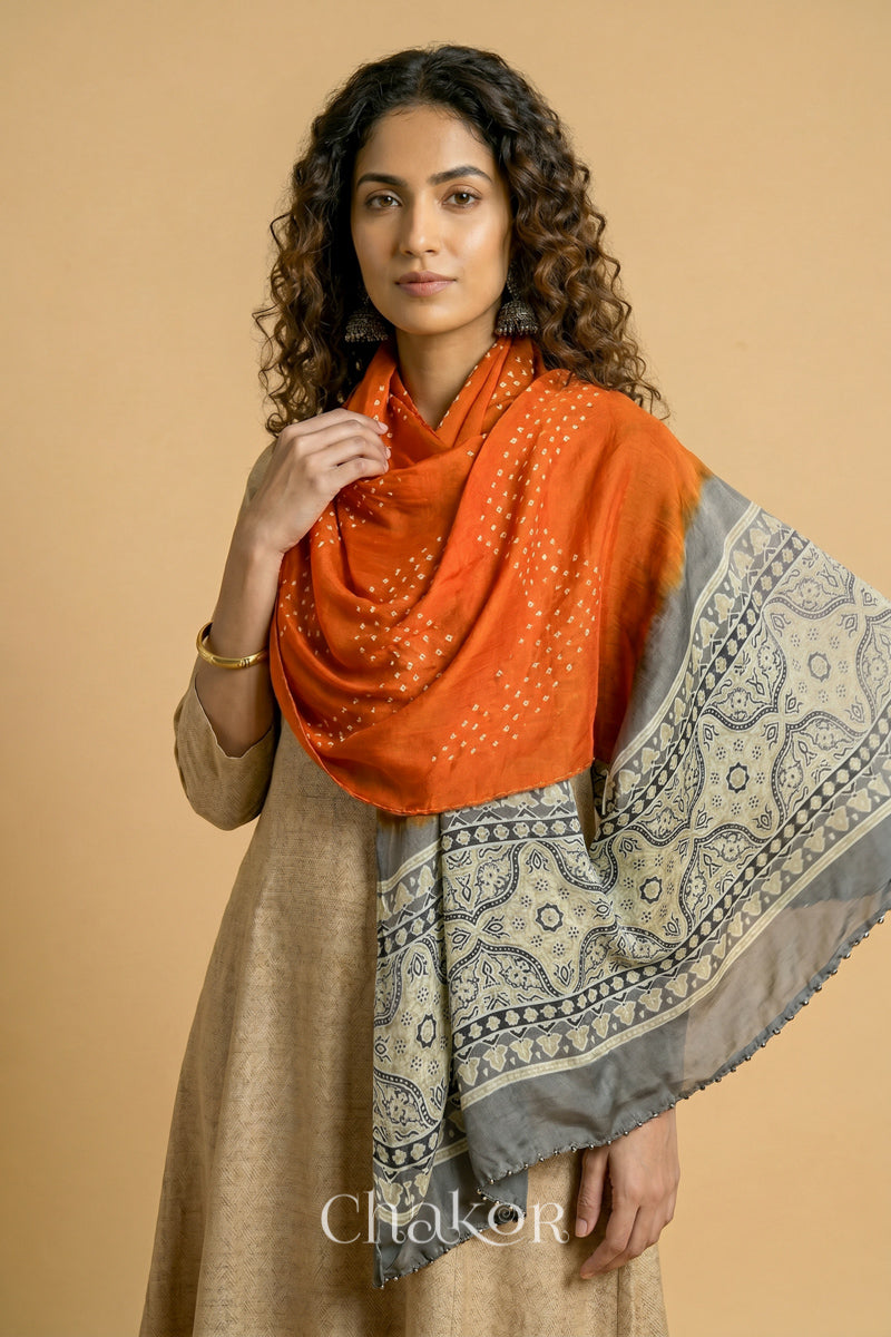 Orange Bandhani modal stole styled across shoulders with detailed Taupe Beige Ajrakh pallu and traditional hand tied pattern.
