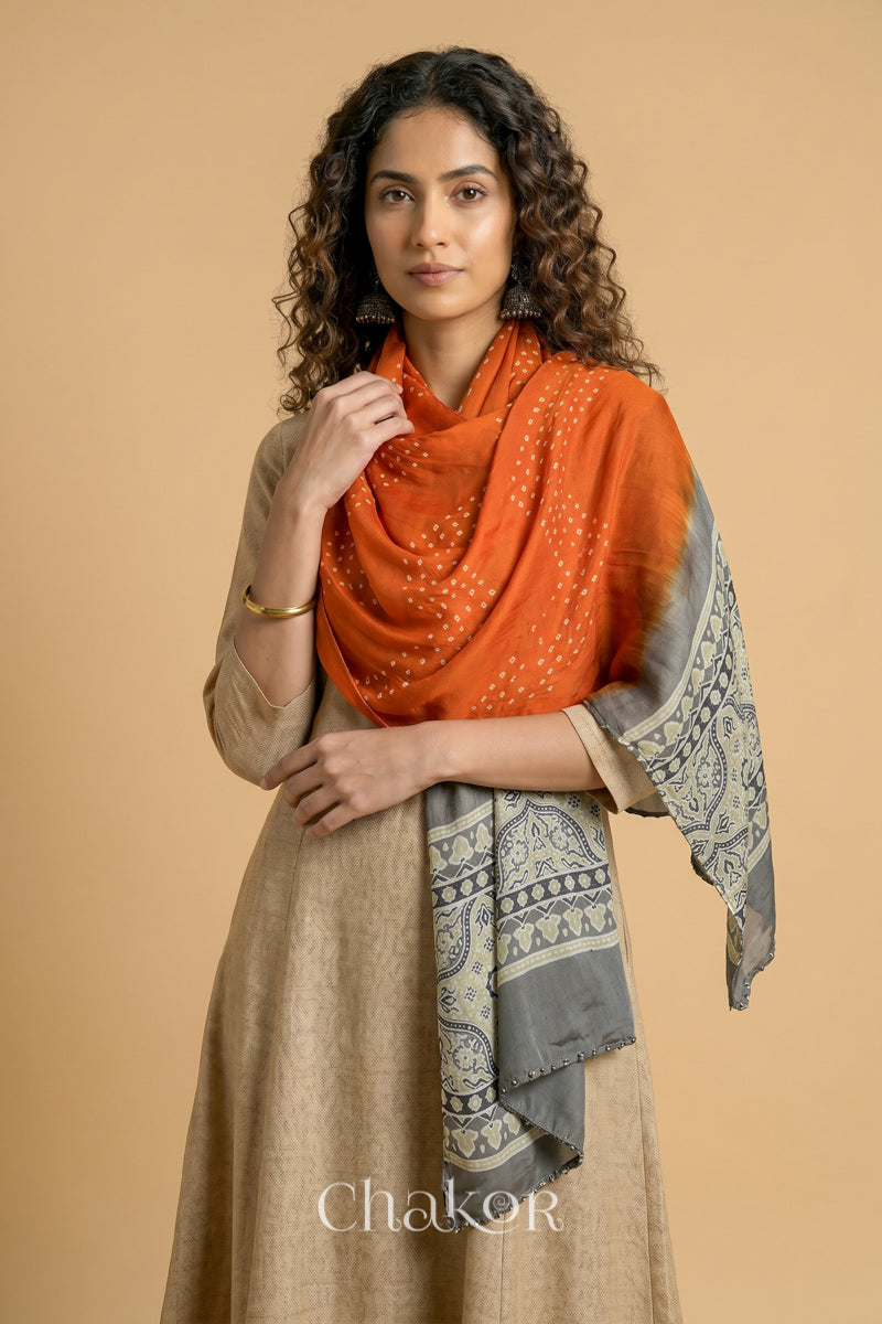 Orange Bandhani modal stole styled across shoulders with detailed Taupe Beige Ajrakh pallu and traditional hand tied pattern.
