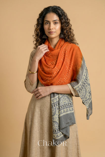 Orange Bandhani modal stole styled across shoulders with detailed Taupe Beige Ajrakh pallu and traditional hand tied pattern.
