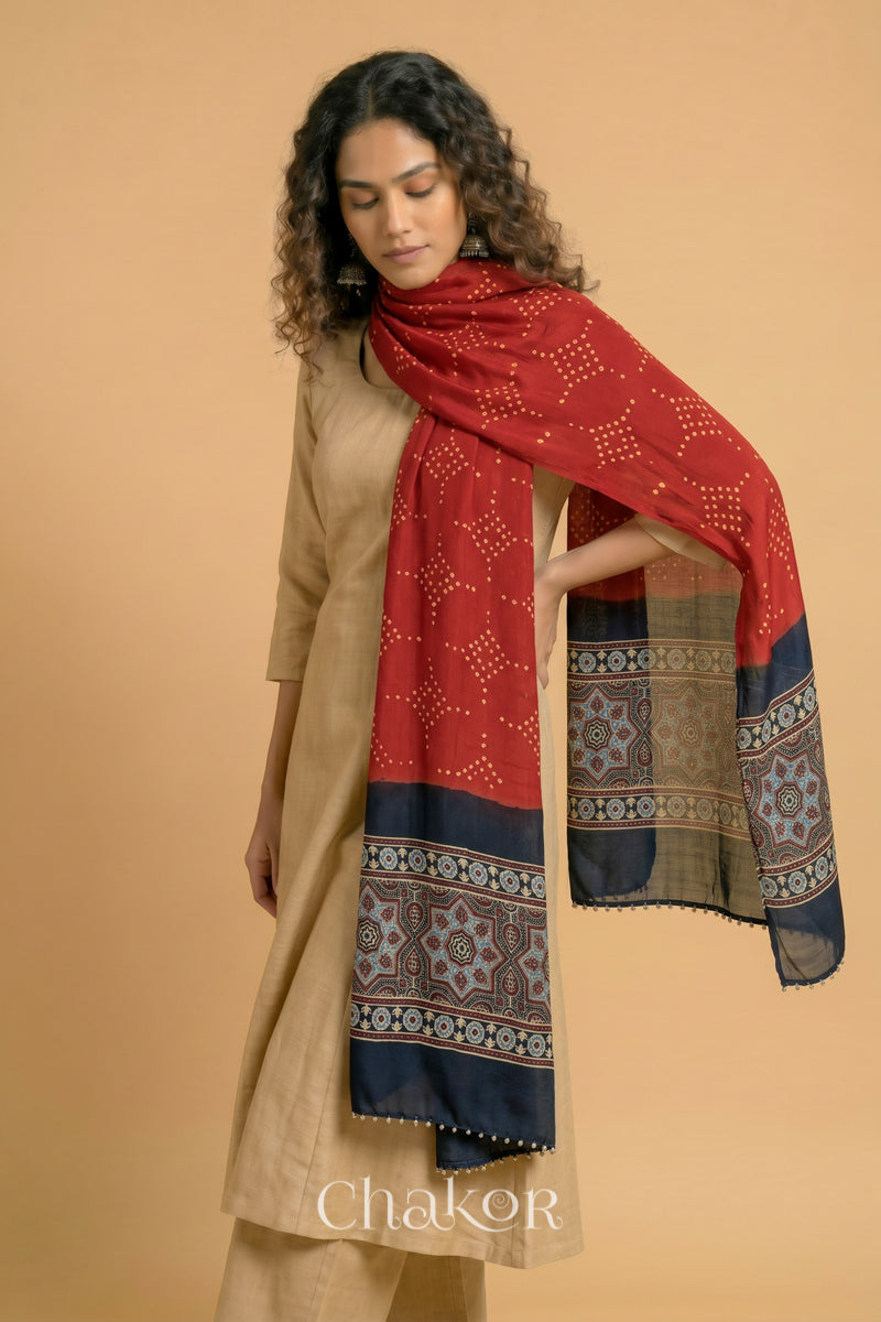 Red bandhani modal stole styled across shoulders with detailed black Ajrakh pallu and traditional hand tied pattern.
