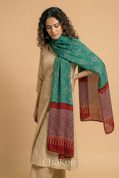 Turtle Green Bandhani modal stole styled across shoulders with detailed Madder Red Ajrakh pallu and traditional hand tied pattern.
