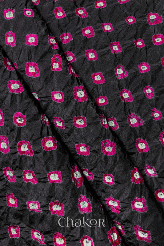 Black Mulberry silk fabric showcasing dual colour Pink bandhani patterns with folds and Chakor brand watermark.
