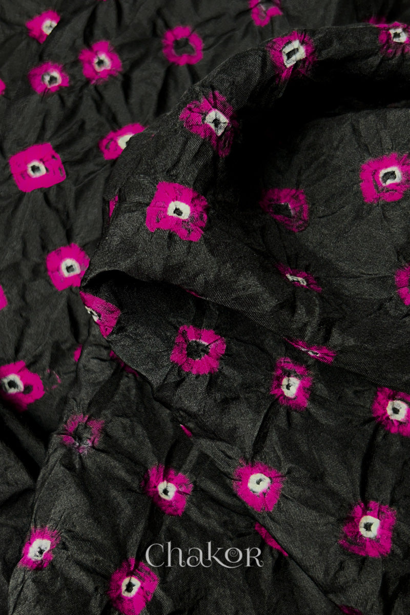 Close-up of Black fabric with Pink and white bandhani patterns, featuring texture and sheen of soft mulberry silk fabric.

