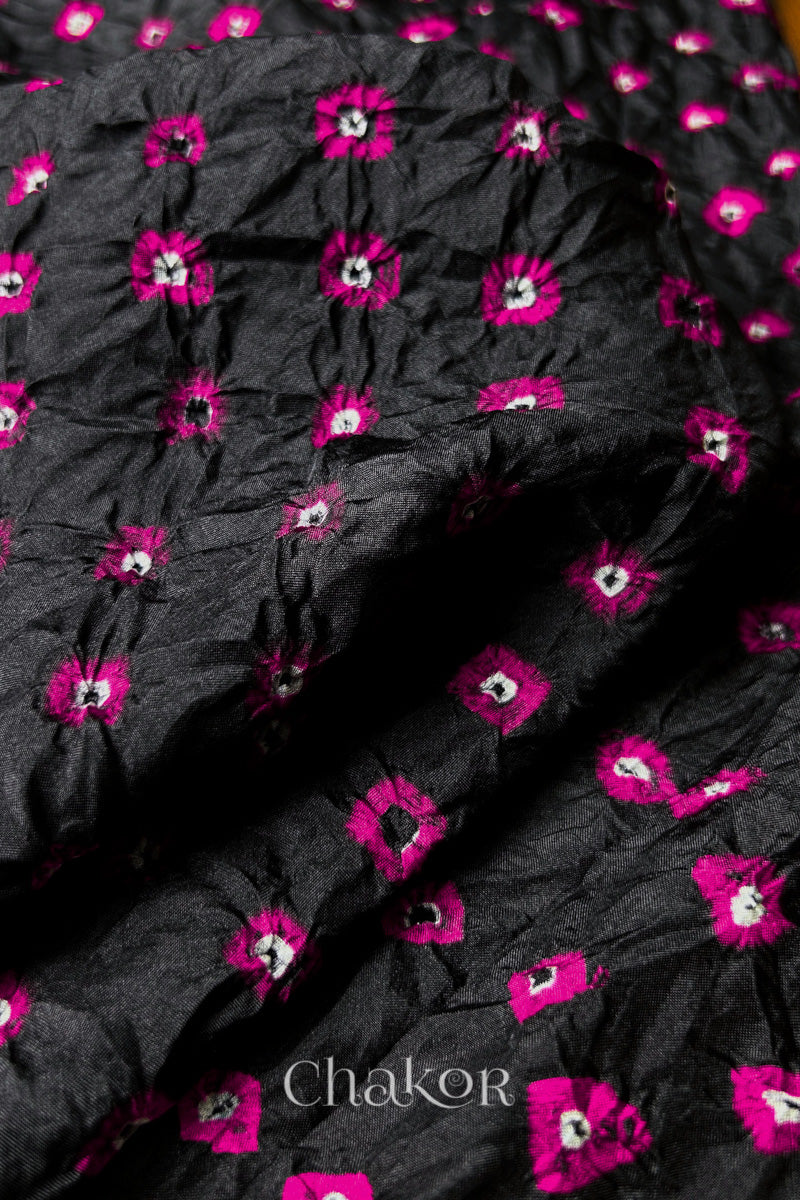 Close-up of Black fabric with Pink and white bandhani patterns, featuring texture and sheen of soft mulberry silk fabric.
