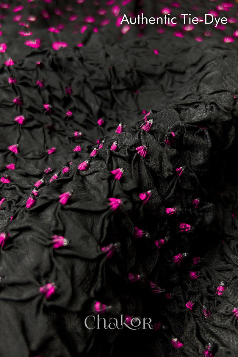 Close-up of Black mulberry silk fabric with Pink and white patterns, featuring texture of authentic bandhani patterns.

