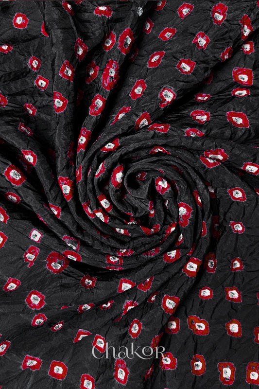 Black Mulberry silk fabric with dual colour Red bandhani dots, arranged in a swirling design  & Chakor brand watermark.
