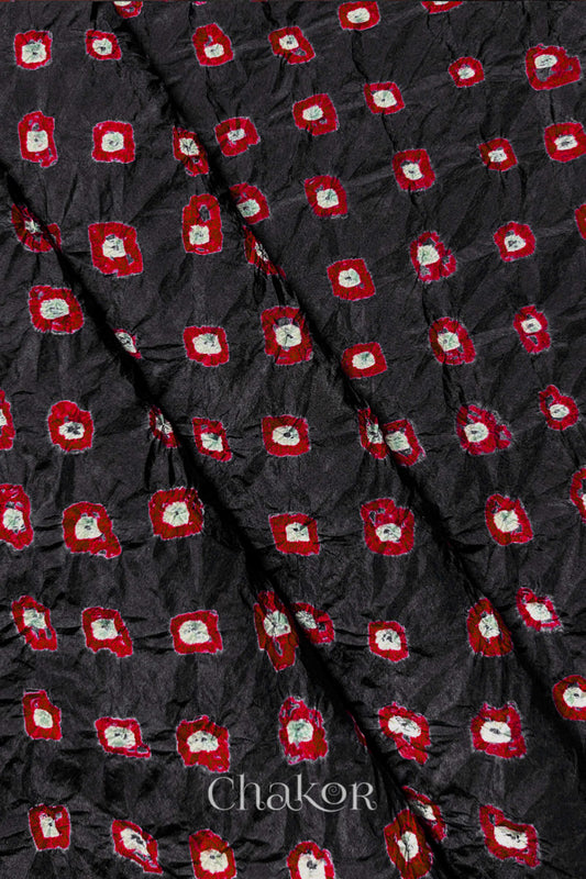 Black Mulberry silk fabric showcasing dual colour Red bandhani patterns with folds and Chakor brand watermark.
