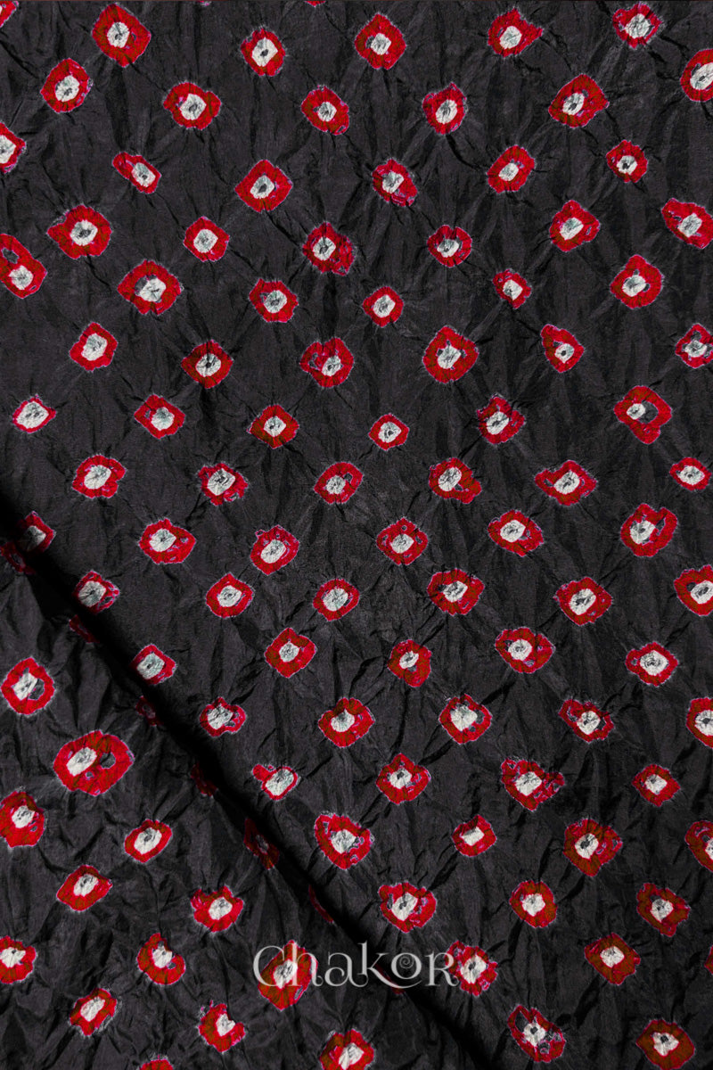 Black Mulberry silk fabric showcasing dual colour Red bandhani patterns with folded corner and Chakor brand watermark.
