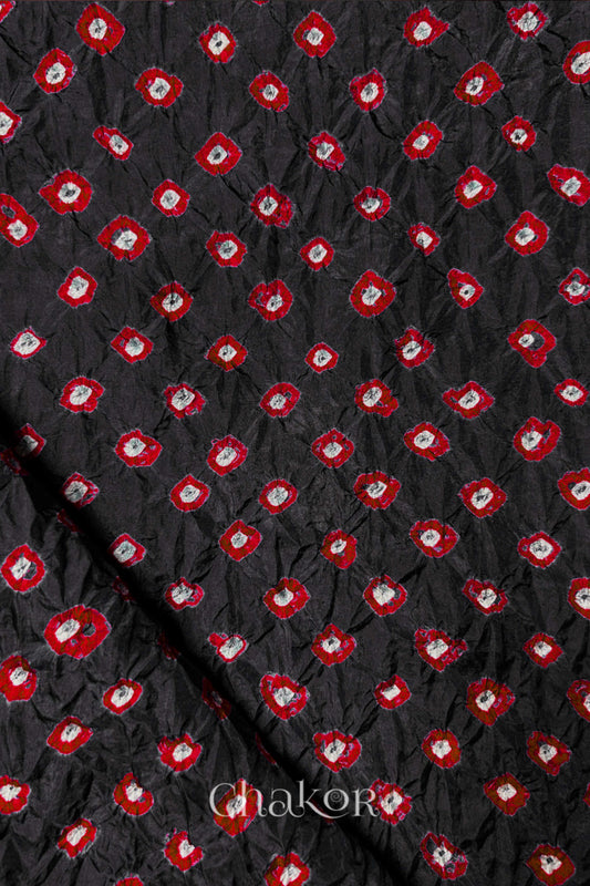 Black Mulberry silk fabric showcasing dual colour Red bandhani patterns with folded corner and Chakor brand watermark.
