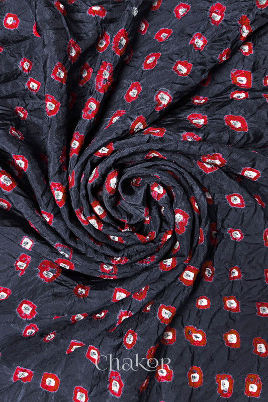Charcoal Grey Mulberry silk fabric with dual colour Red bandhani dots, arranged in a swirling design  & Chakor brand watermark.
